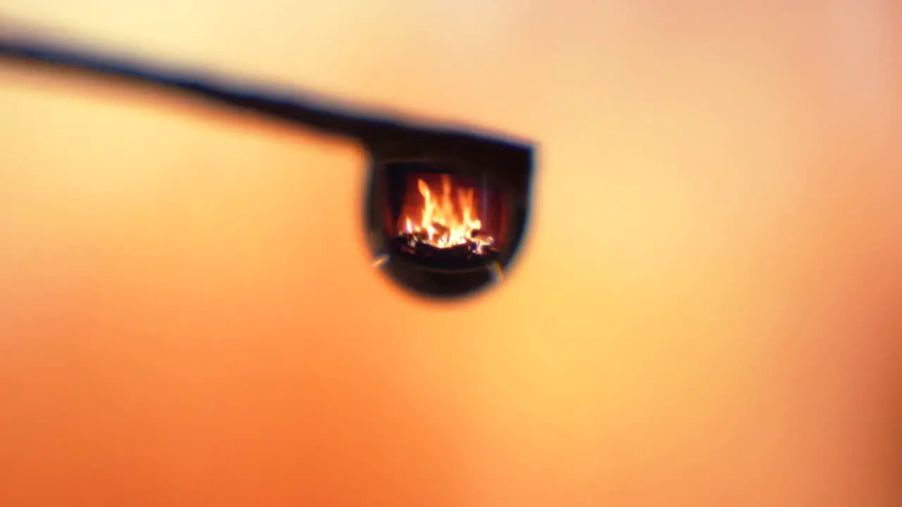 Zoom in shot single droplet fireplace reflection flames burning background