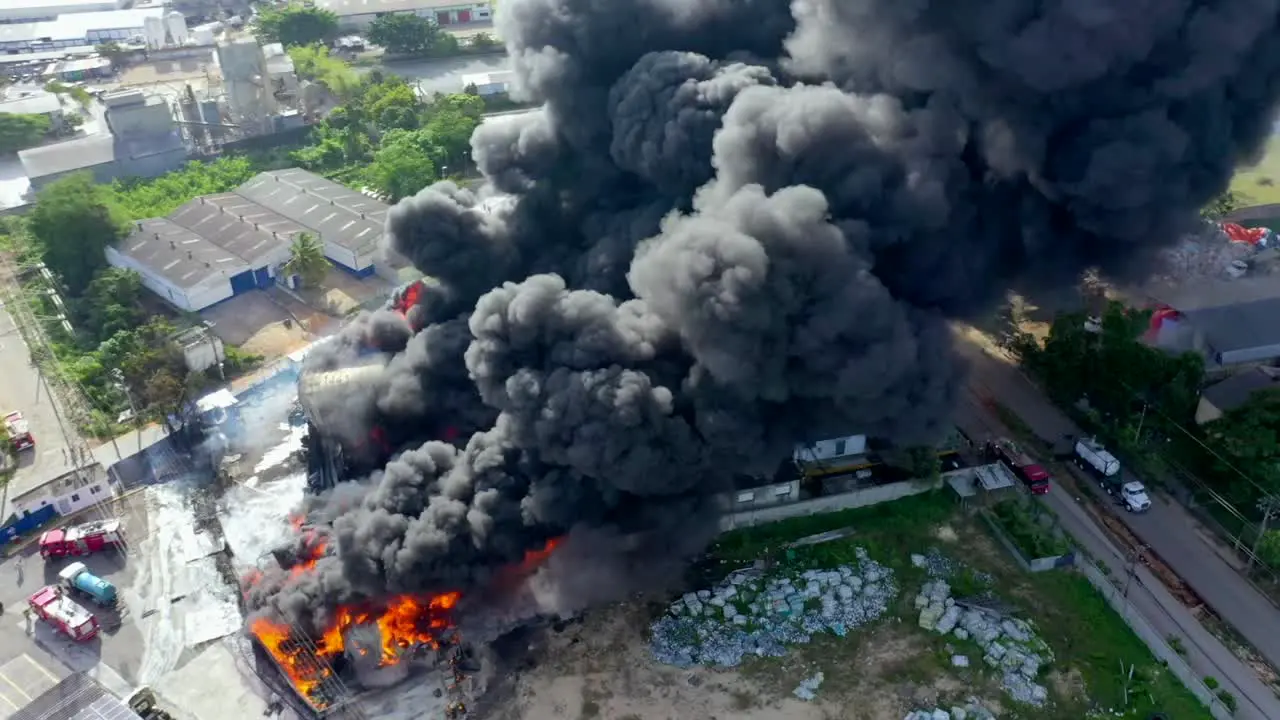 Flying Close Over a Massive Devastating Fire as it Consumes Large Commercial Warehouse Building Creating Huge Thick Black Smoke Cloud during Daytime