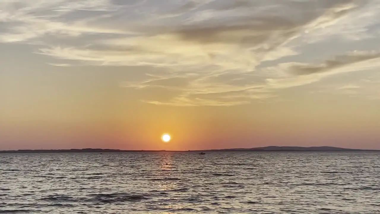 Orange sun over wavy waters during summer sunset and small boat passing