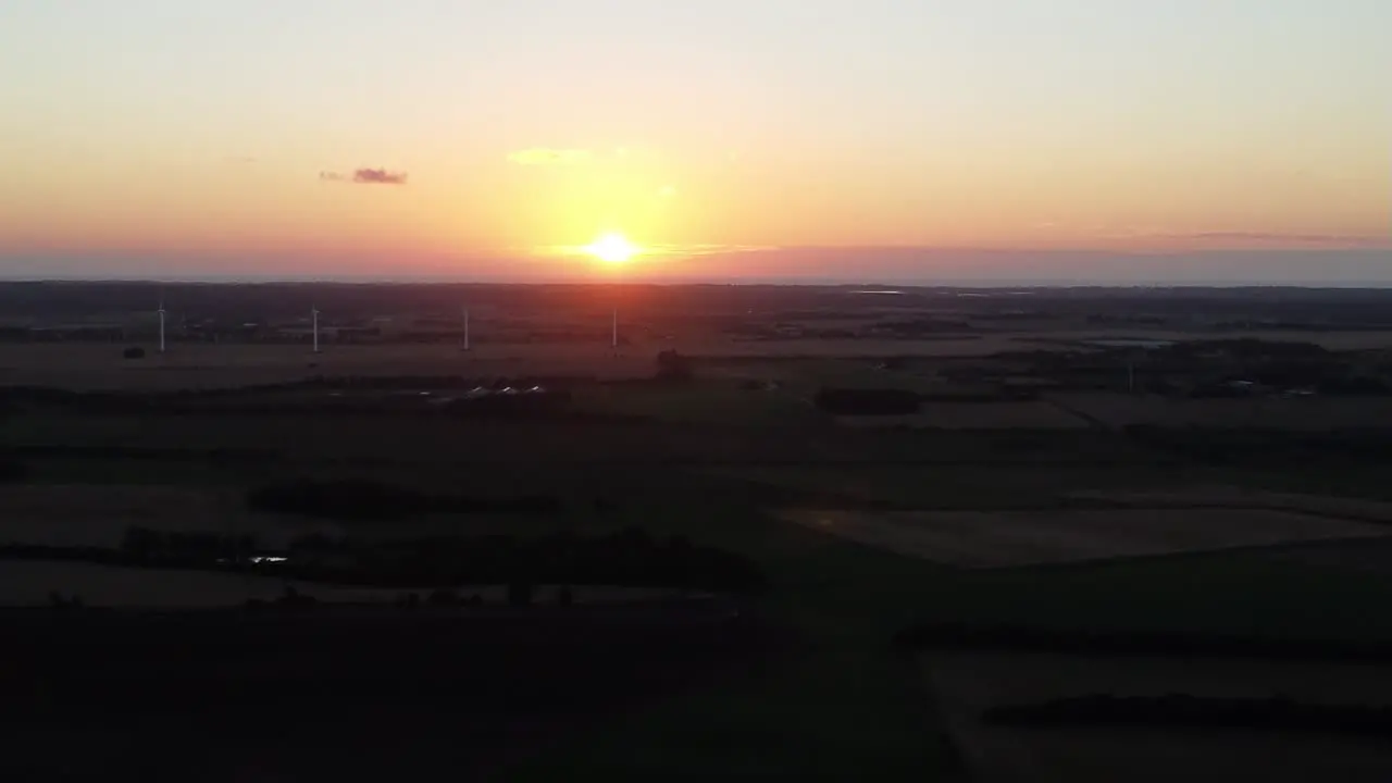 Drone flies to sunset with lush green farm landscape on the ground in snedsted