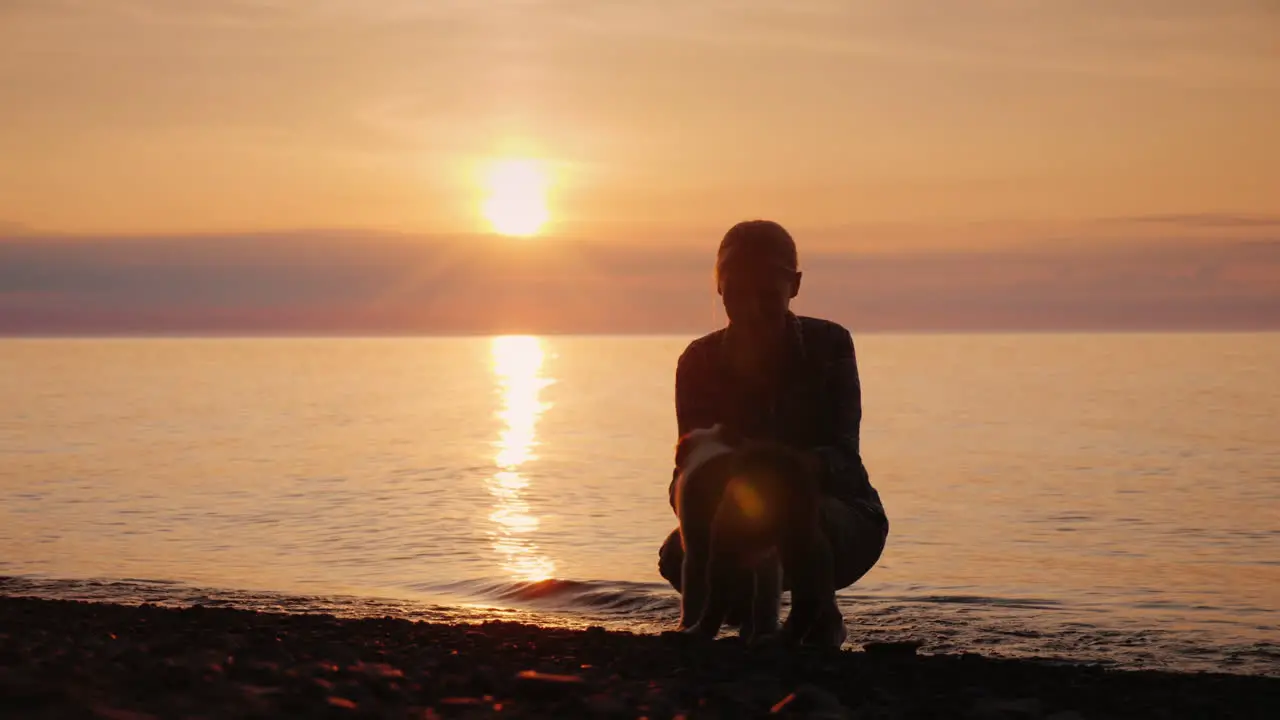 Woman Playing With A Dog By The Lake At Sunset