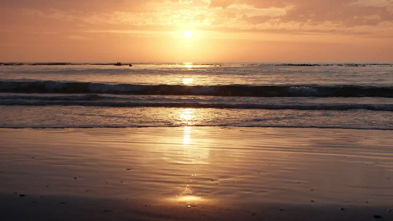 Golden sunrise reflects on the sandy beach as waves ripple