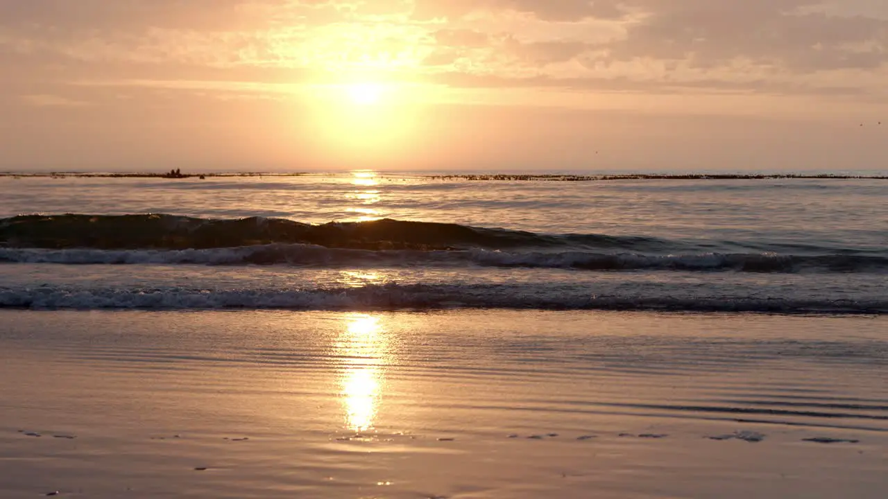 Golden sunrise reflects on the wet beach as waves break and wash onto shore gently