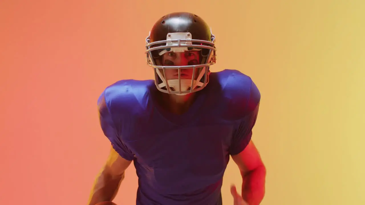 Video of close up of caucasian american football player in helmet with ball over orange background