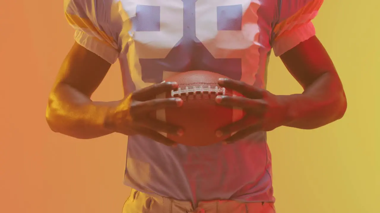 Video of midsection of african american american football player with ball over orange background