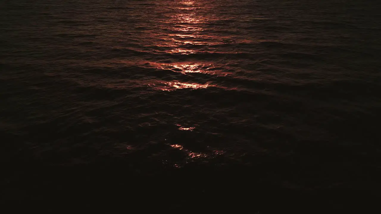 Aerial flight over the open sea ocean by sunset with the red and orange sunlight reflecting on the water and waves in slow motion