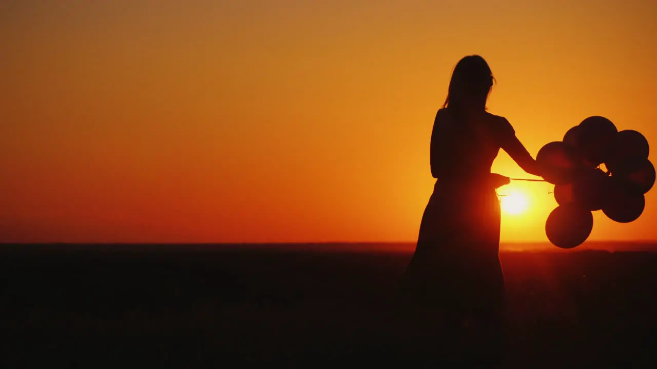 Silhouette Of A Woman Carelessly Spinning With Balloons In Her Hand At Sunset