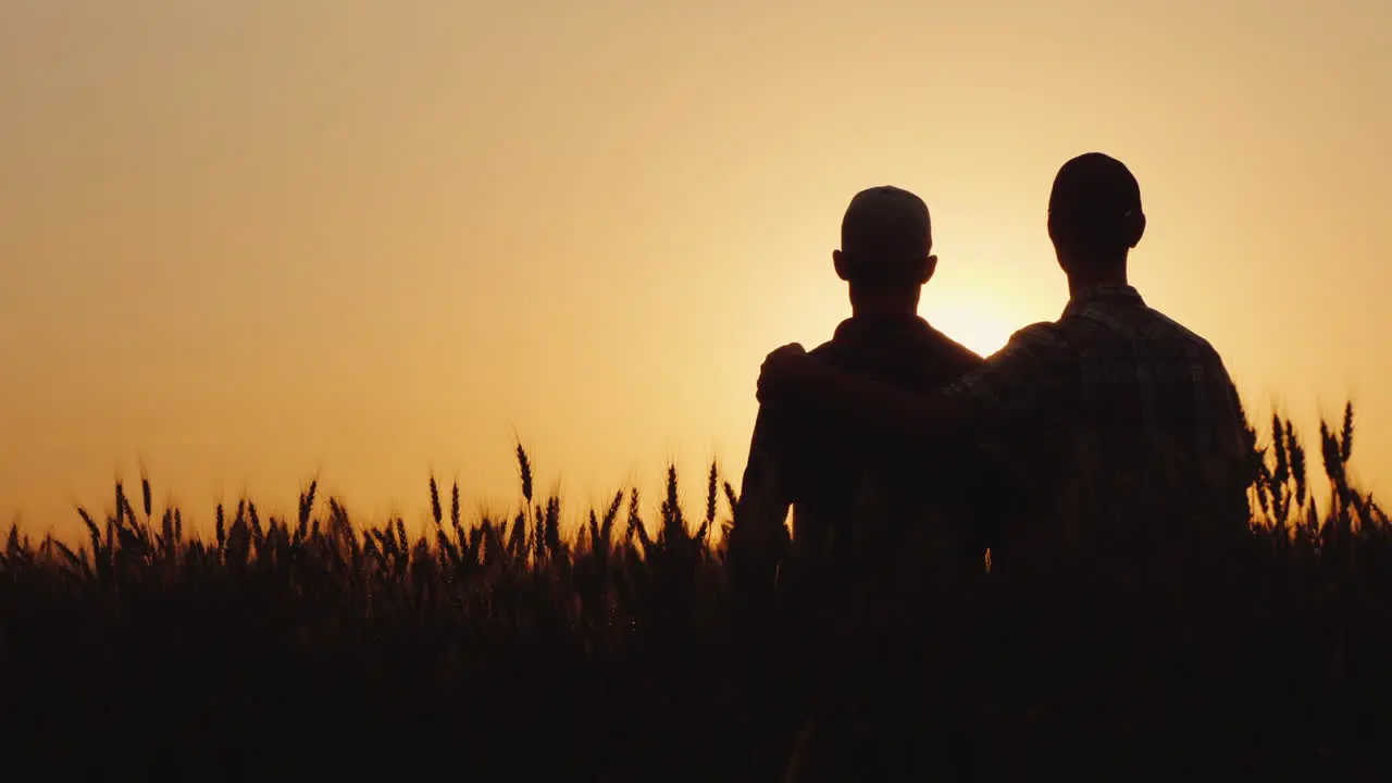 Two Gay Men Stand Hugging At Sunset Looking Forward To The Horizon