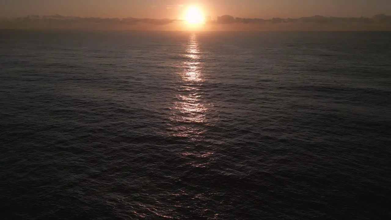 Tropical sea aerial drone tilting up reveal a beautiful golden sun rising from the sea with colorful cloudy sky and sunbeams