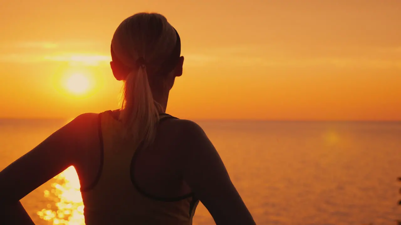 Purposeful Female Athlete Looks At The Sunset Over The Sea Rear View