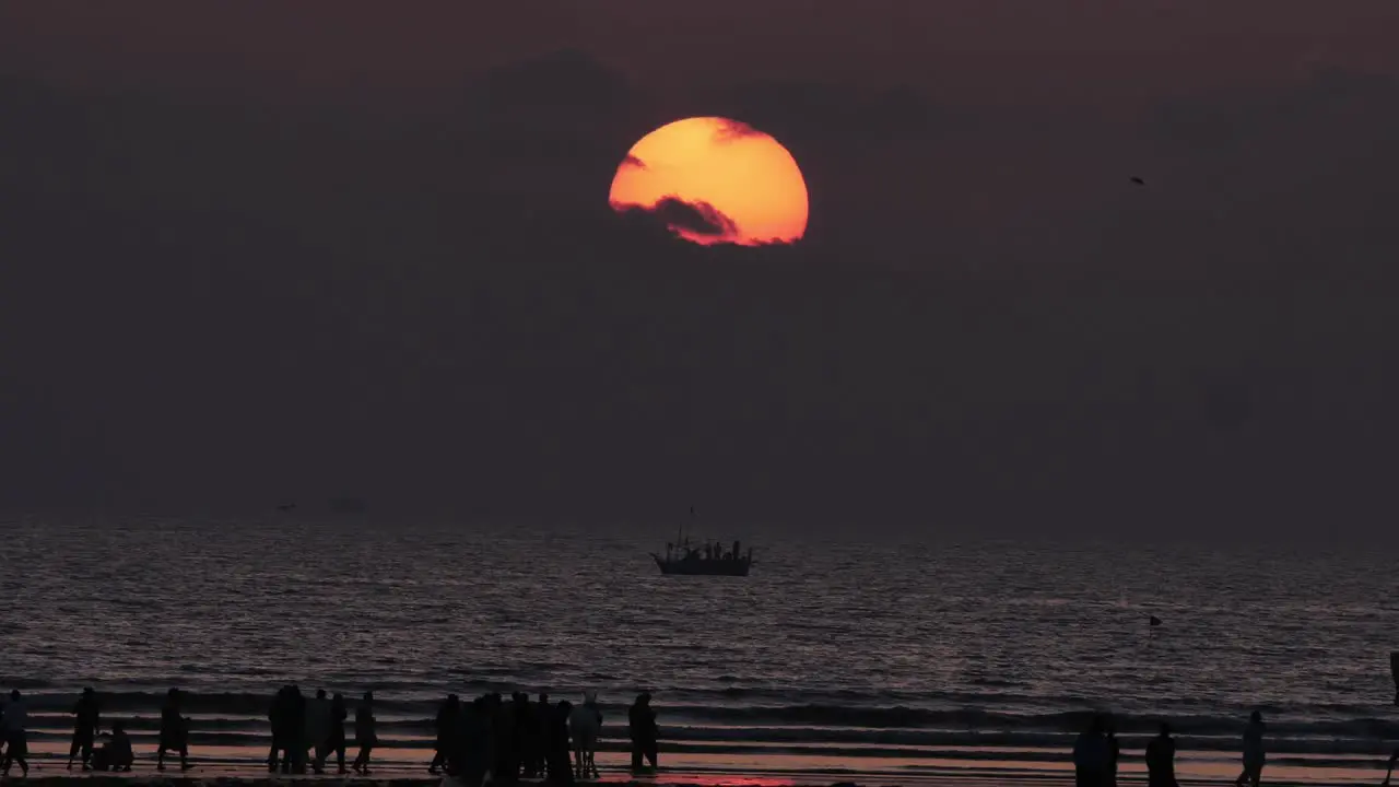 Orange Sun and Sunset Skies Slow Zoom Out Reveal Of Silhouette Of People On Karachi Beach