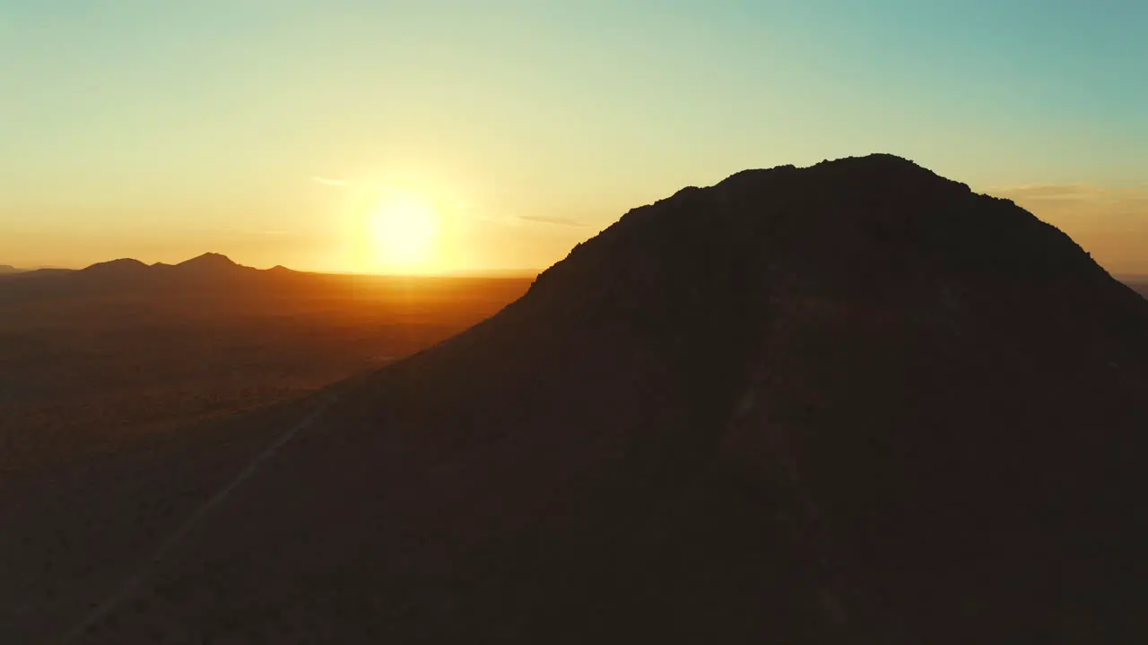 Flying from behind a mountain peak in the Mojave Desert to reveal the sun then orbiting around the mountain for an aerial view of the vast landscape