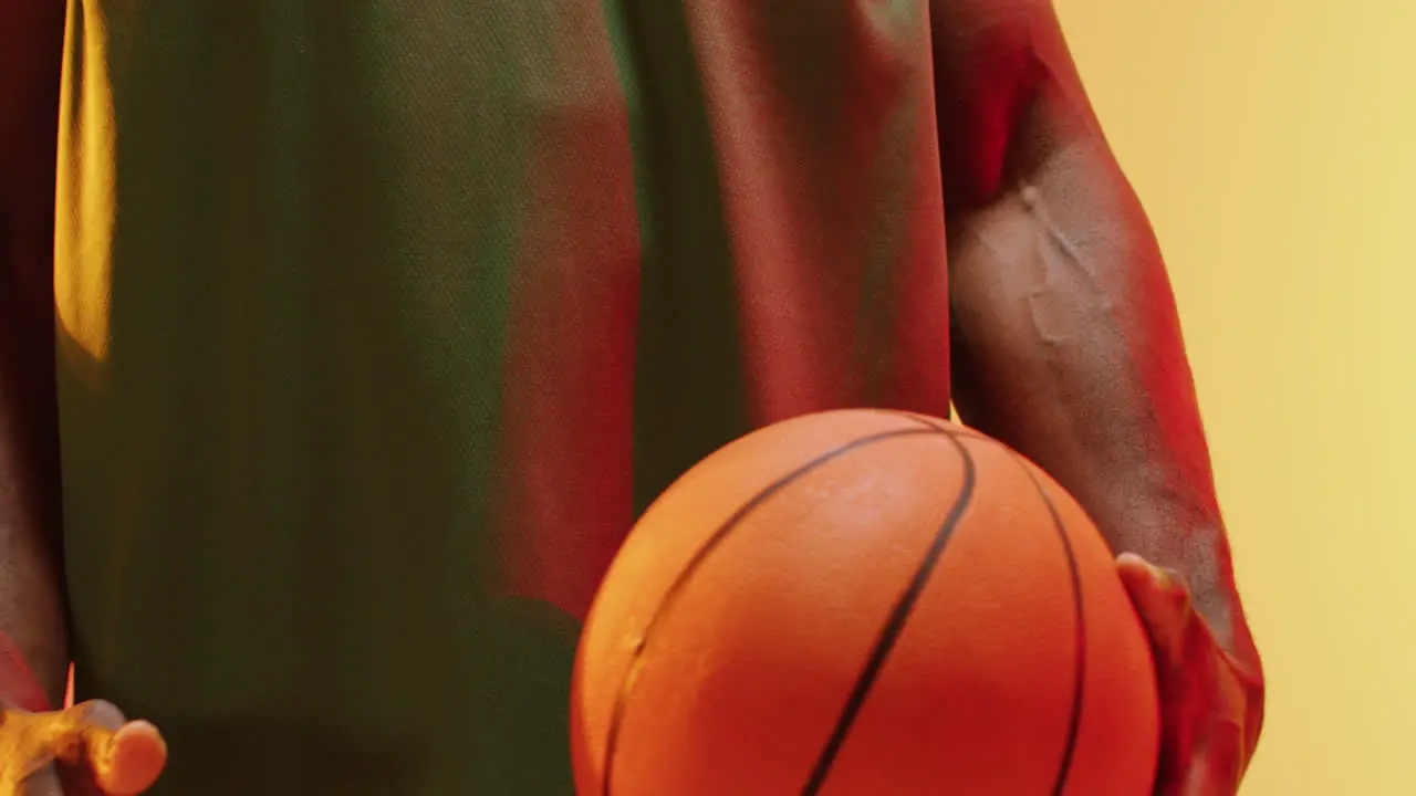 Video of midsection of african american male basketball player holding ball on orange background