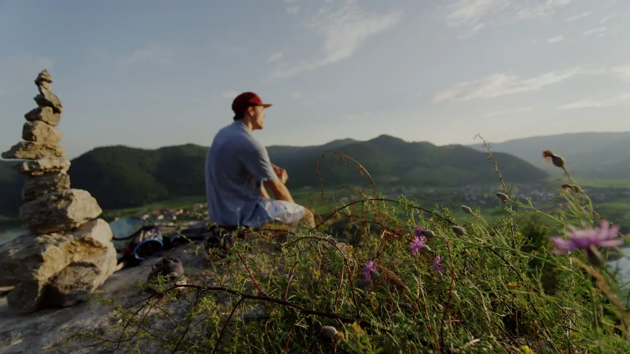 peaceful mountain picknick place man having a break in flowerfield stone tower enjoying the view taking in the sight landscape overview cinematic slow motion slomo male guy enjoys outdoor hills