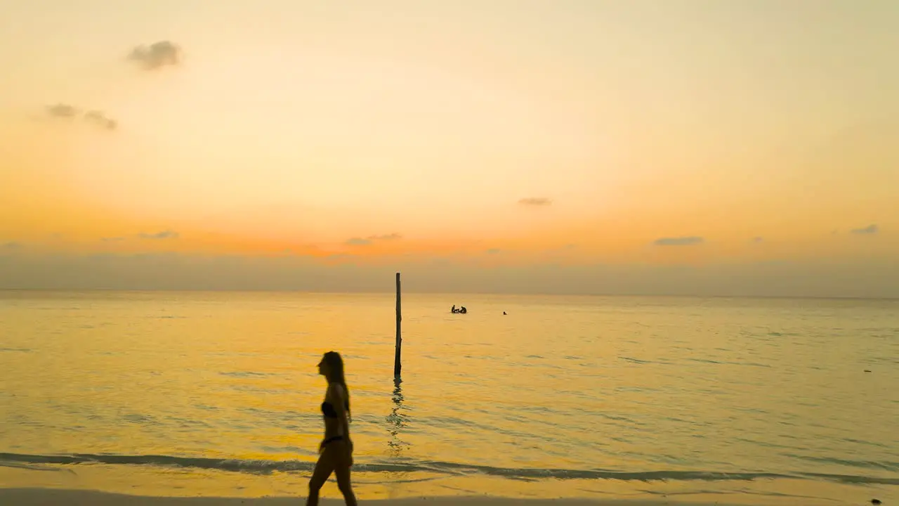 Aerial woman in wetsuit walking on beach during orange sunset maldives