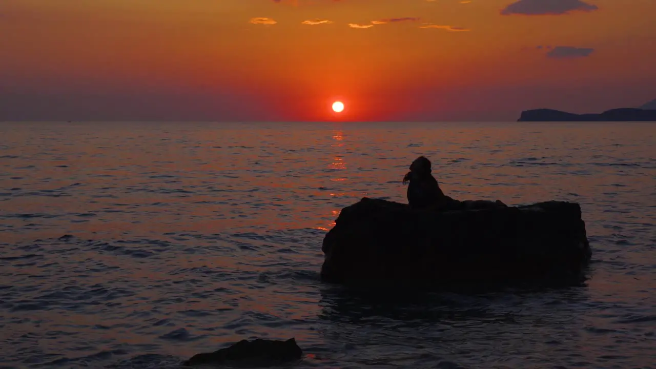 Spiritual exercises of Yoga executed by girl on cliff surrounded by sea at beautiful sunset with sun on red sky