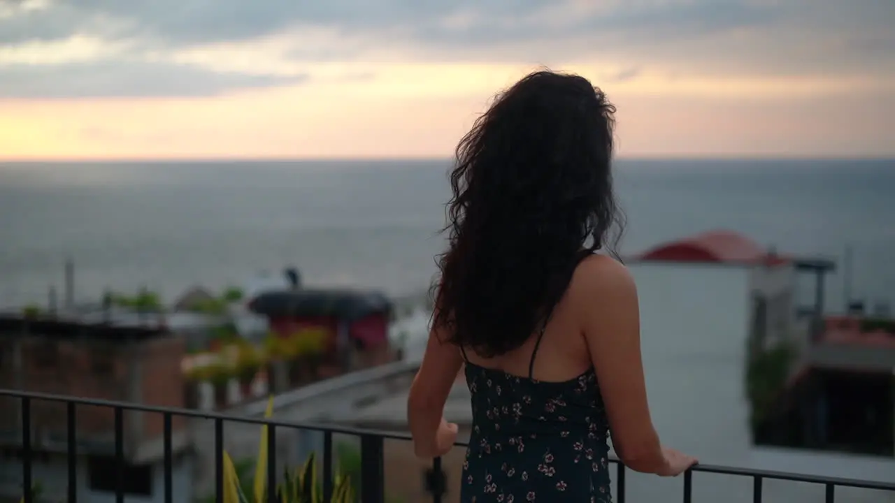 Young brunette woman watching the sunset over the ocean from the rooftop pull back rack focus