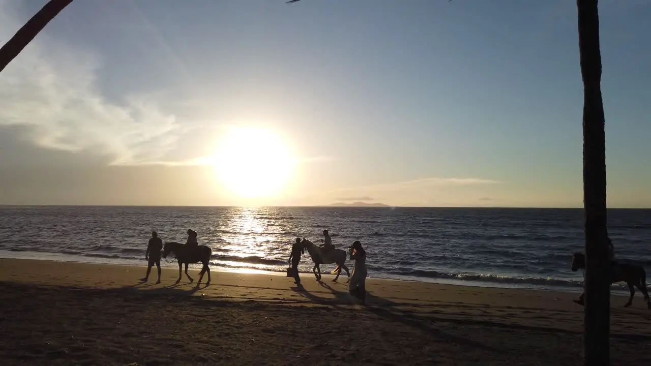 Horses riding on golden sandy Fiji beach with tropical island sunset coastline as background