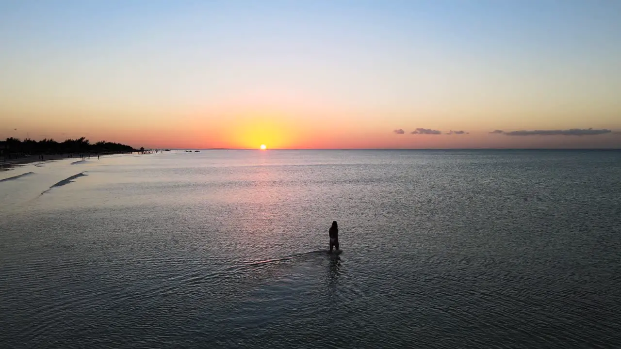 Wide angle drone shot of a beautiful young women walking in the shallow water off the beaches during sunset of the tropical island of Holbox in Mexico shot in 4k