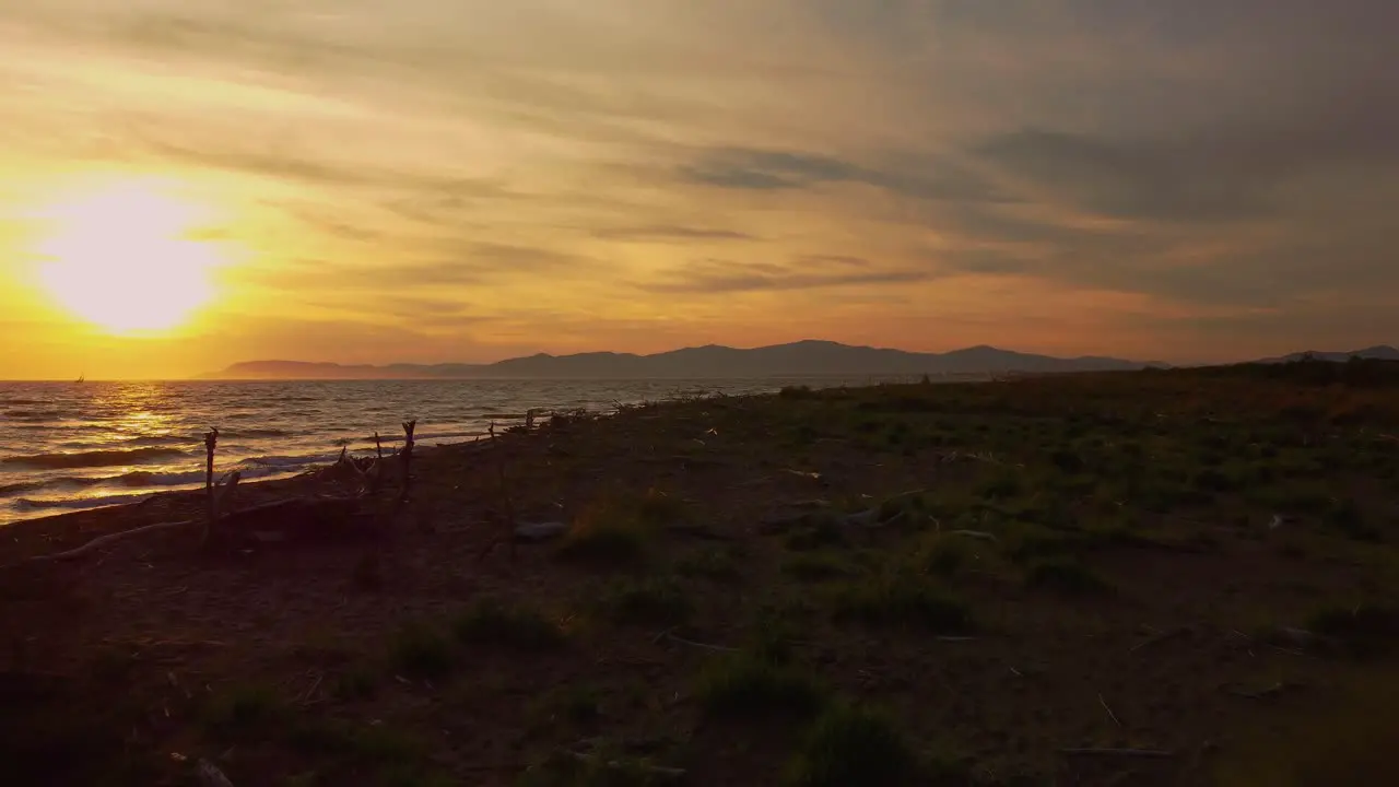 Slow cinematic low aerial drone footage of the sunset at a sandy beach at the seaside near Alberese in the iconic Maremma nature park in Tuscany Italy with waves islands and a dramatic red sky