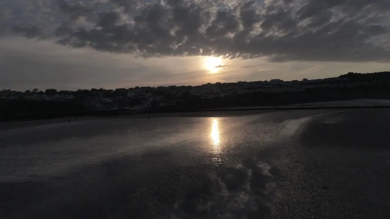 Evening cloudy golden sunset colours across Benllech beach silhouette coastline Anglesey aerial view slow pull back