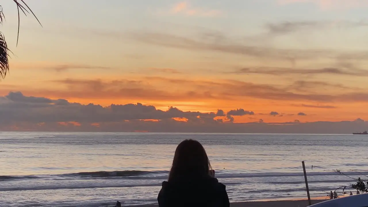 Slow motion of people at Carcavelos beach Slowly waves form and break beautiful Atlantic ocean deep yellow sunset on water reflections Portugal