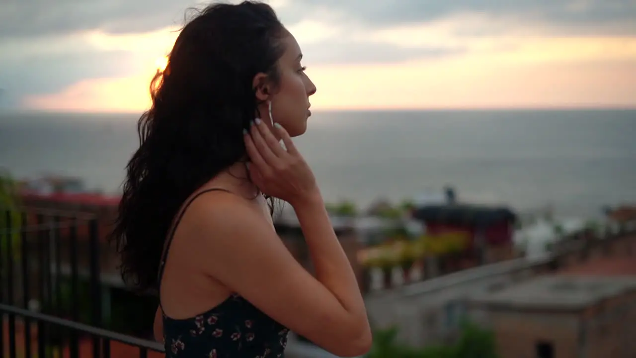 Beautiful young woman on vacation takes in the sunset ocean and view of the town from the rooftop