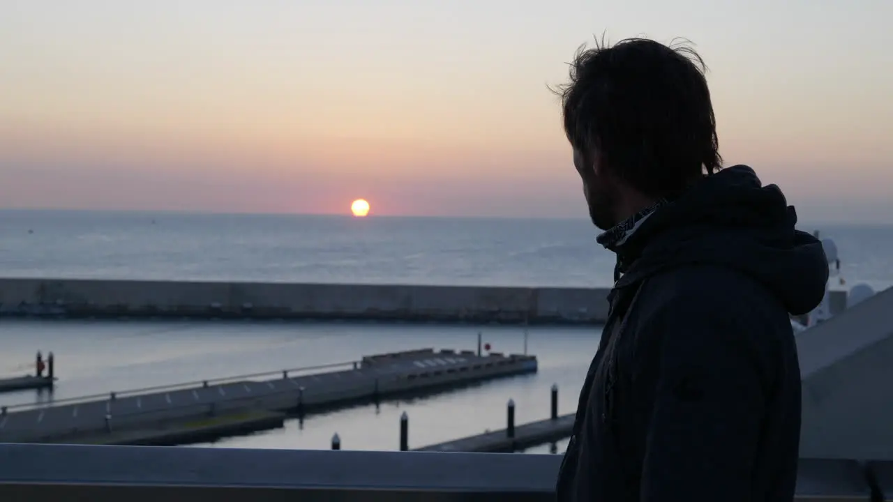 Casual man walking Barcelona marina bridge alone watching the sunset over the ocean