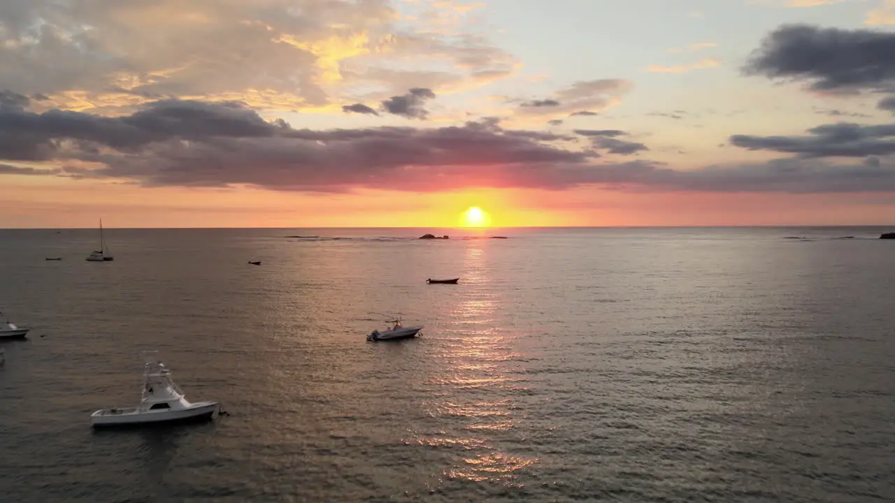 Anchored boats on calm waters dramatic clouds illuminated by a low fiery golden sun aerial pan up