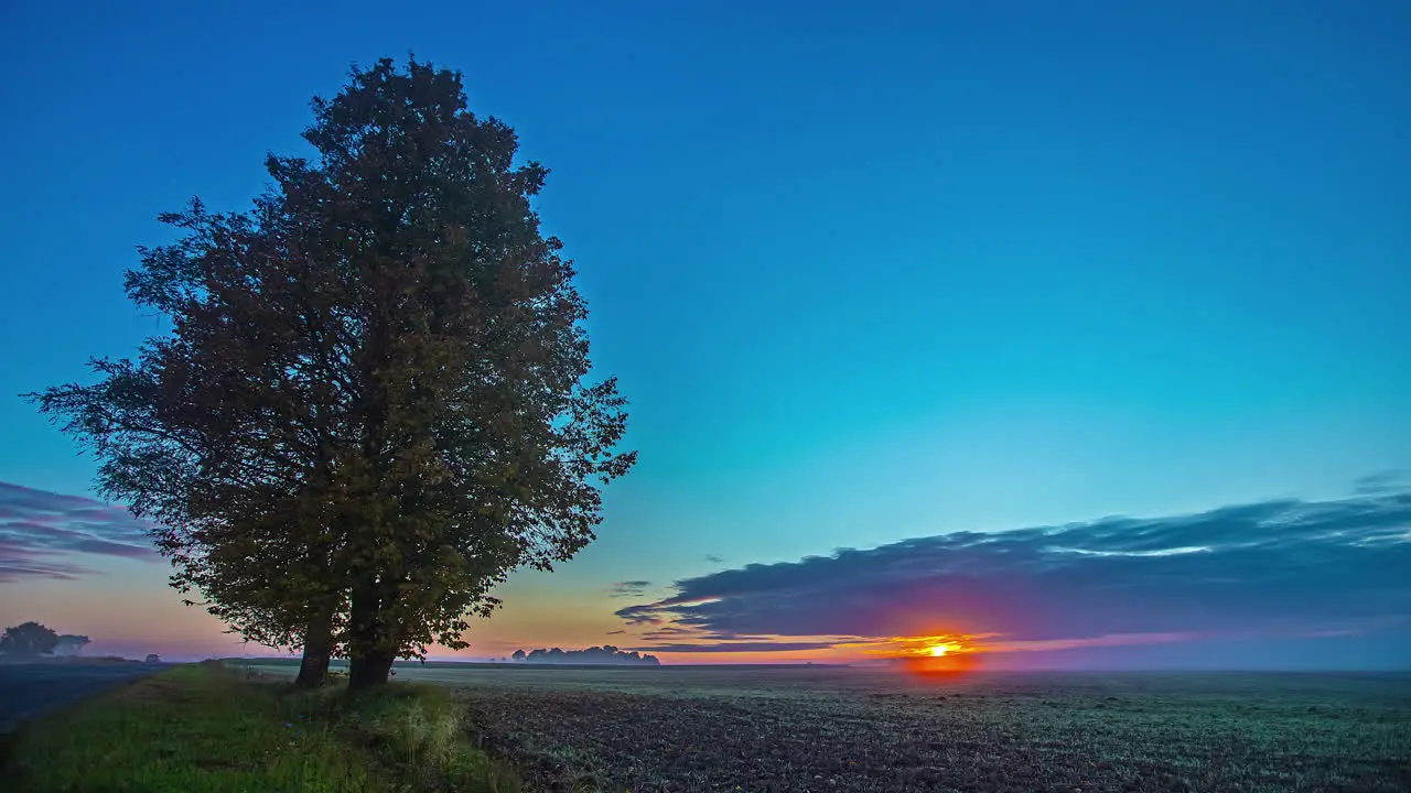 The golden glow of a sunset over a farmland field in the European countryside wide angle time lapse