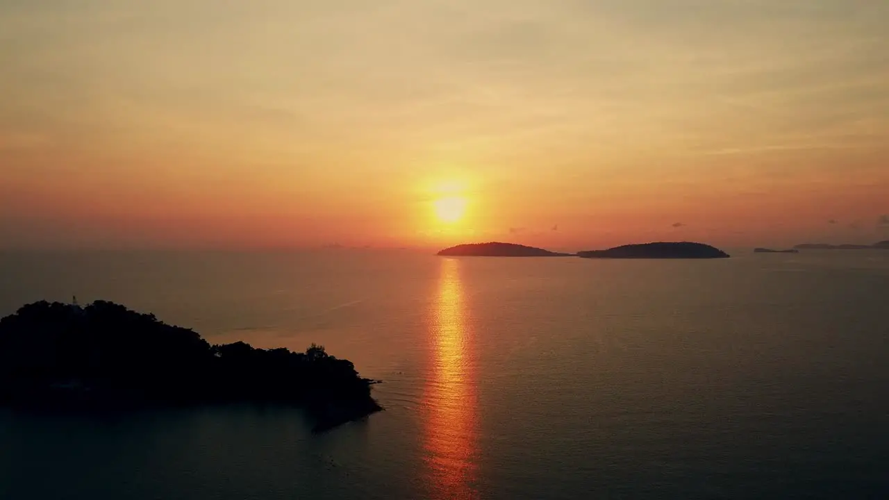 Aerial view of a beautiful sunrise behind the mountains island over the ocean and flying smooth over the sea in the morning viewpoint nature landscape of Thailand