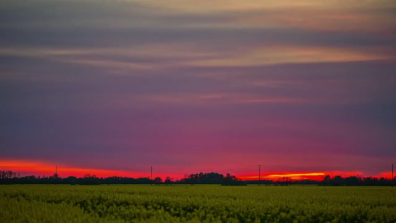 time lapse of a sunset with an orange sky over a green meadow