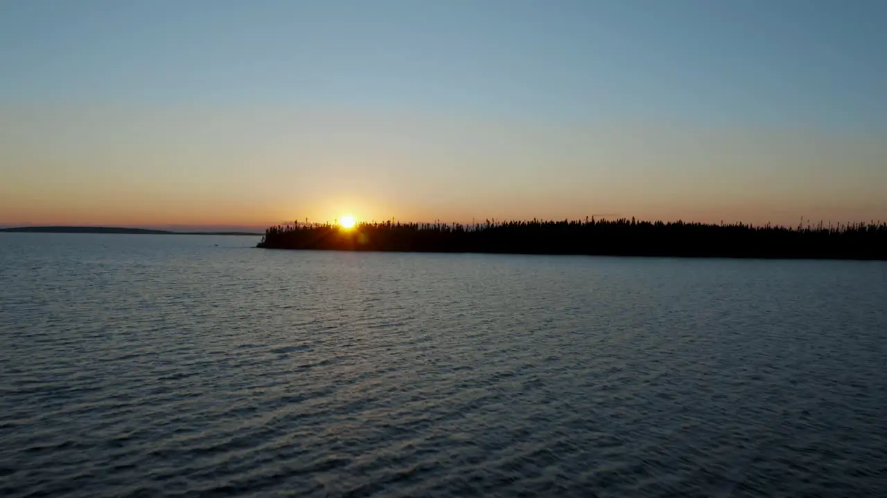 Drone flying along the water of a lake and slowly moving up to reveal a pretty sunset