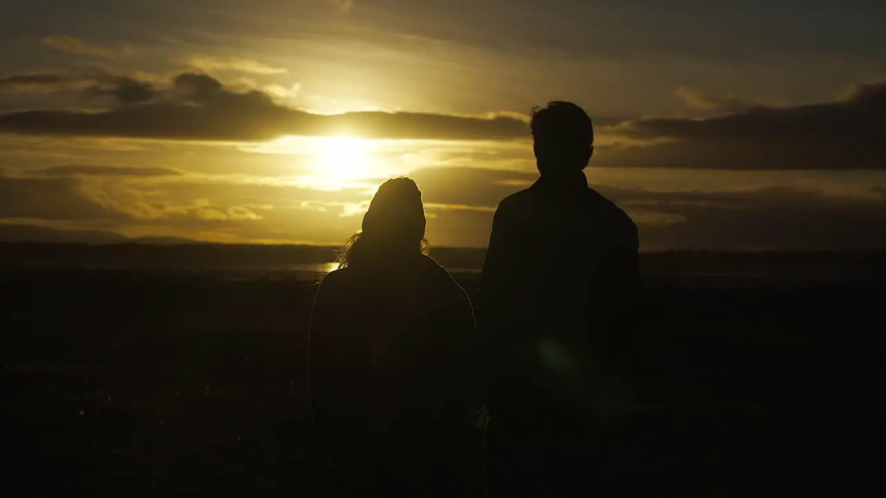 Silhouetted couple in love admiring beautiful sunset by sea rising above grass