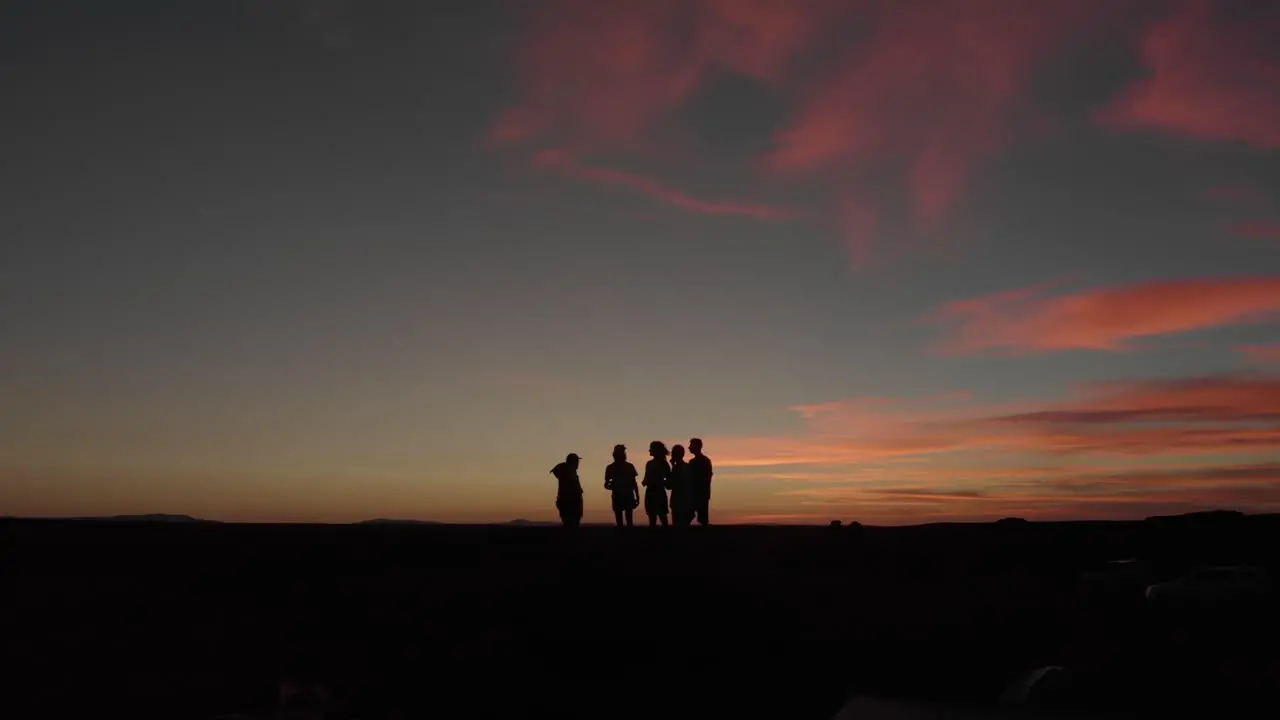 Aerial flight by group of friends as silhouette against desert sunset