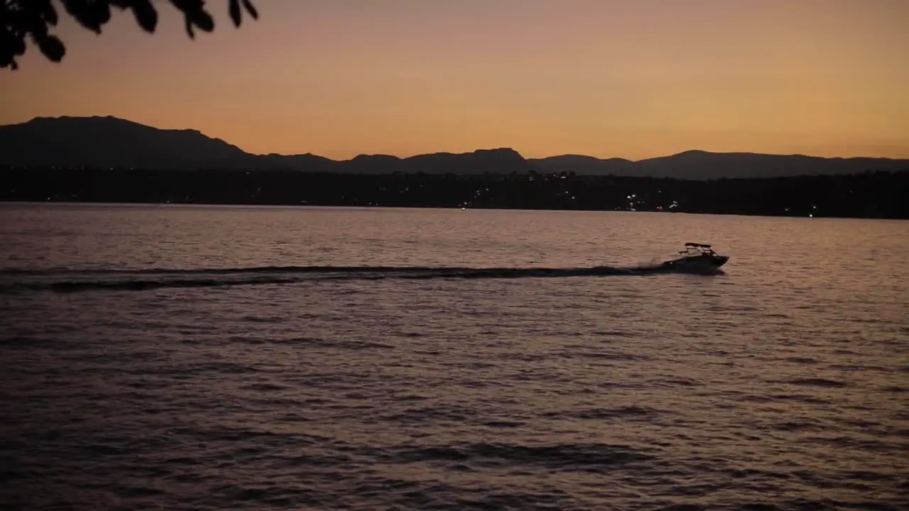 Boat cruising through the waters of a lake on a clear evening with the mountains in the back