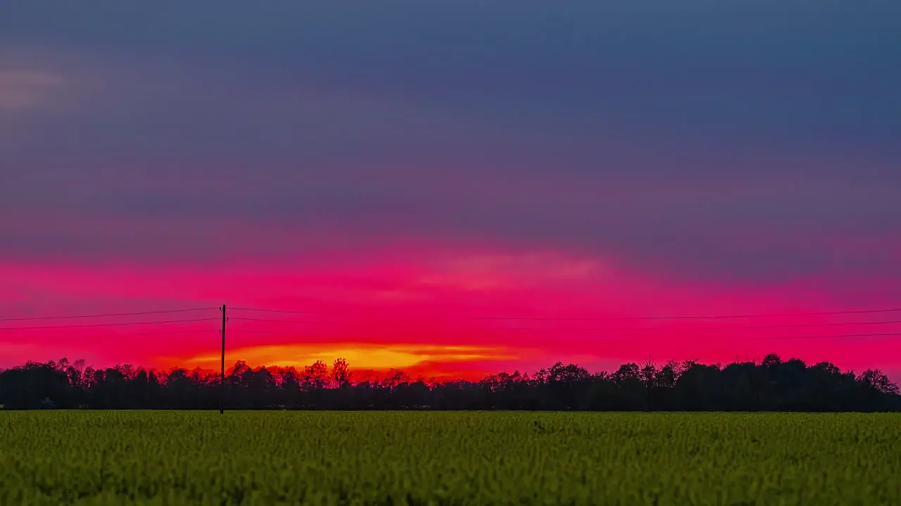 Dramatic sunset through colorful sky with green field in the foreground timelapse