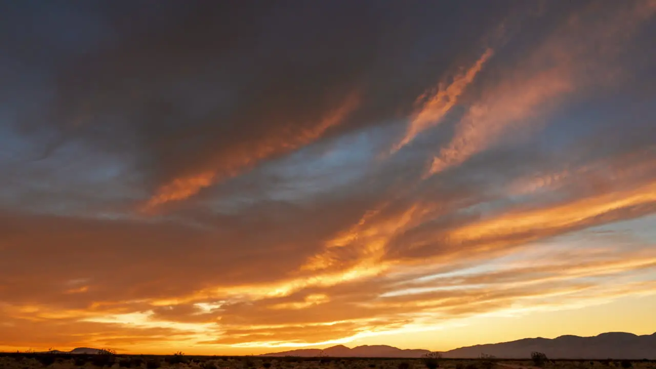 The sky glows from gold to brilliant red over the Mojave Desert as the sun sets beyond the western mountains wide angle time lapse