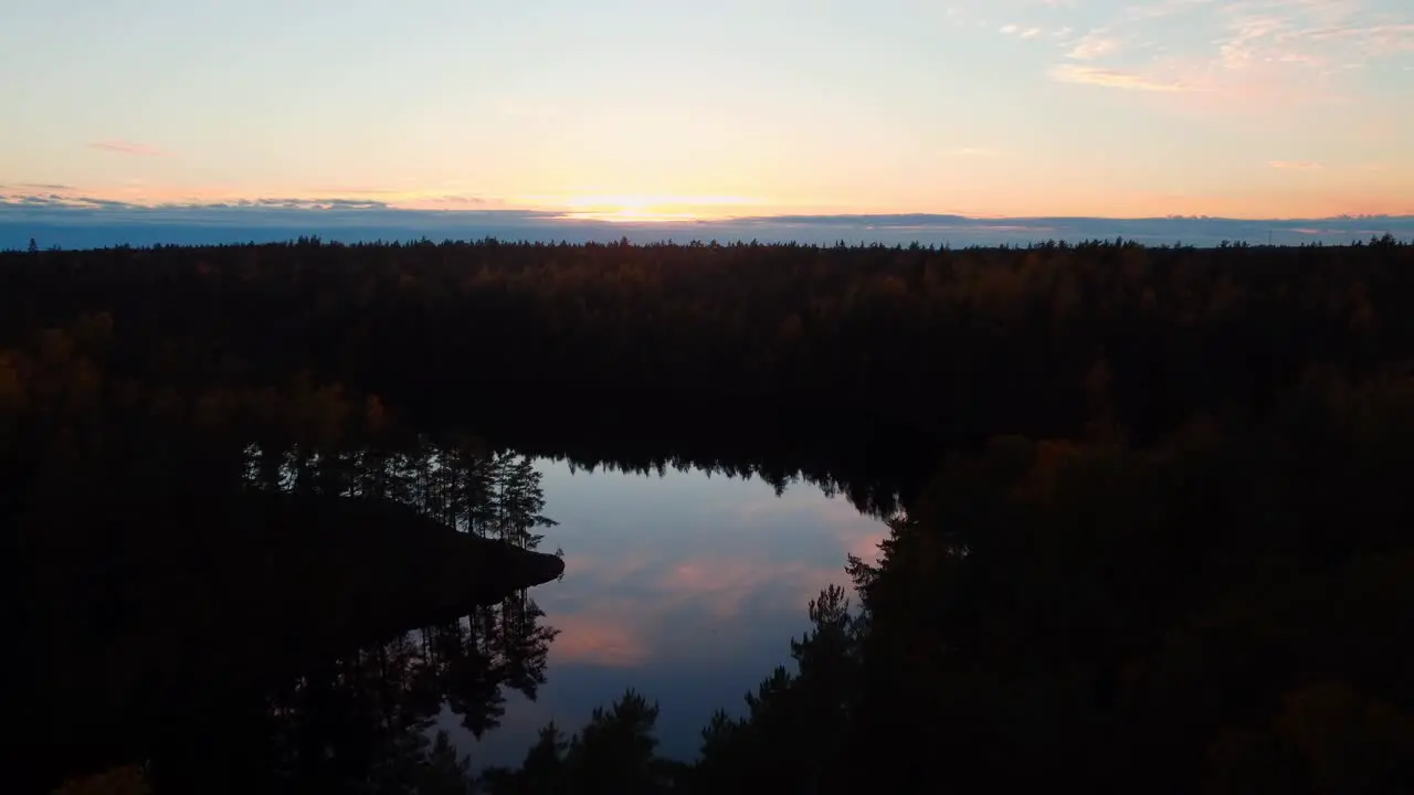 flying at sunset over dark forest as the sky of pink clouds reflects in the lake