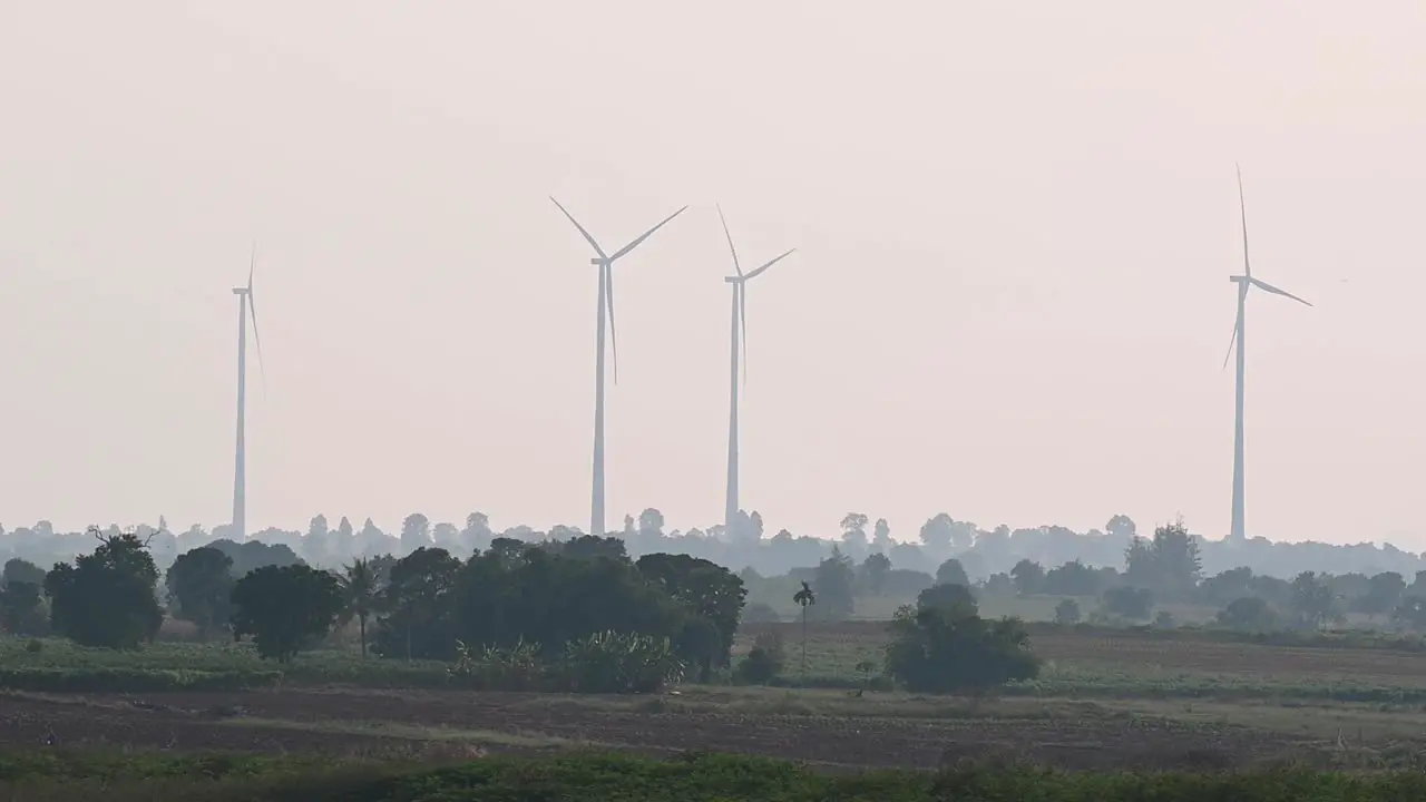 Wind Turbines spinning in the afternoon as farmlands with trees create a lovely silhouette of a landscape and a Crow flies from the left to the right