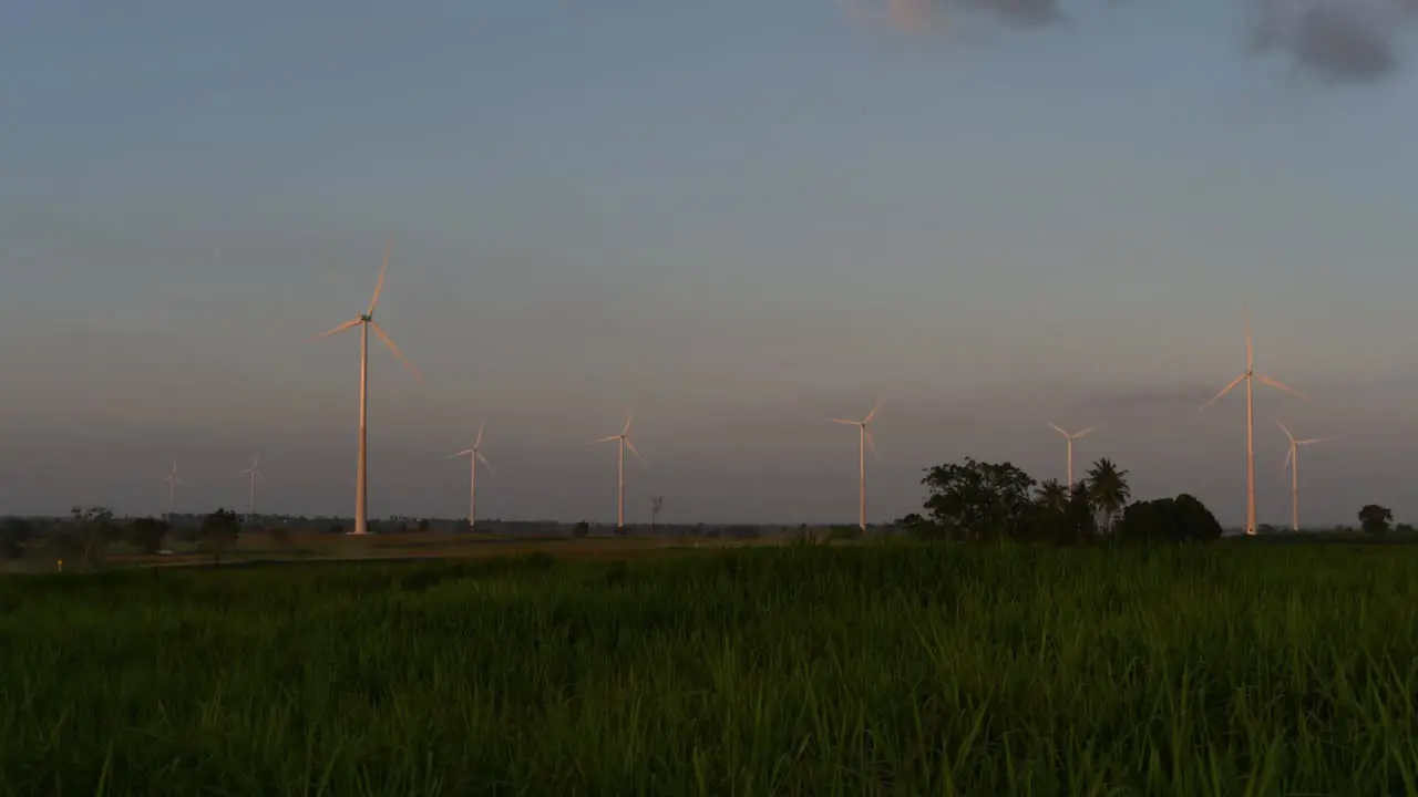 Wind Turbines shooting out of a Farmland while the Sun is setting as Trucks Pass by making Clouds of Dust clean alternative energy in Thailand and mainland Southeast Asia