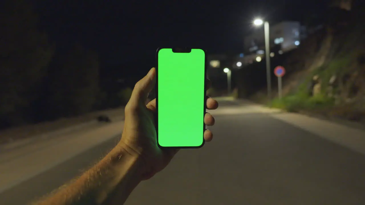 Engaging Nighttime POV Man's Hand Holds iPhone 14 with Greenscreen on Empty Street Lit by Lamps Chroma key