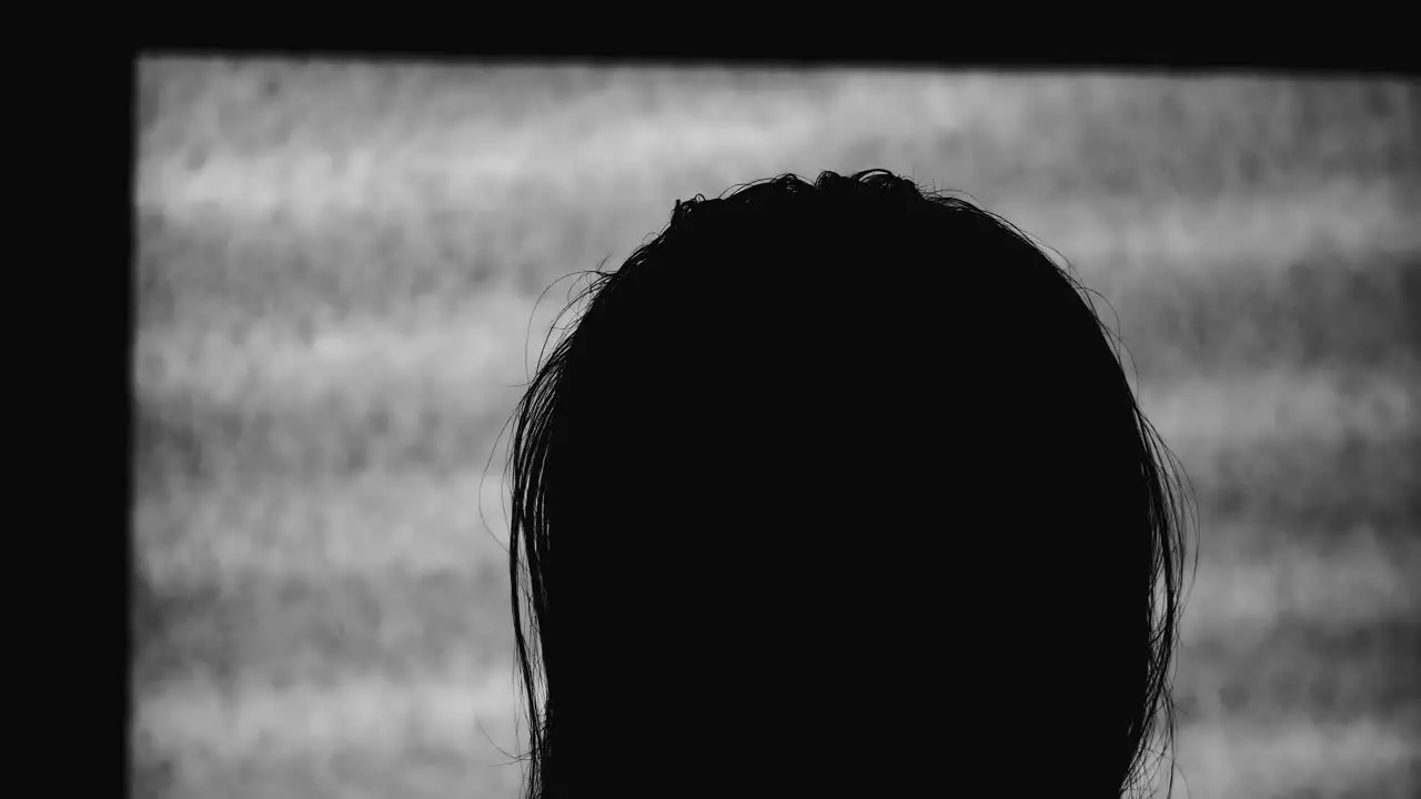 In dark room a mysterious person watches tv that is only displaying static