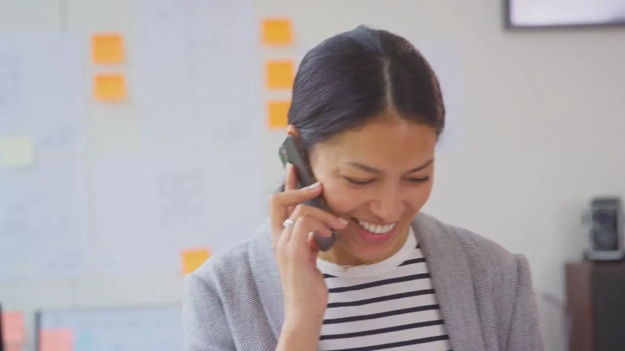 Businesswoman Working In Office Standing At Desk Talking On Mobile Phone