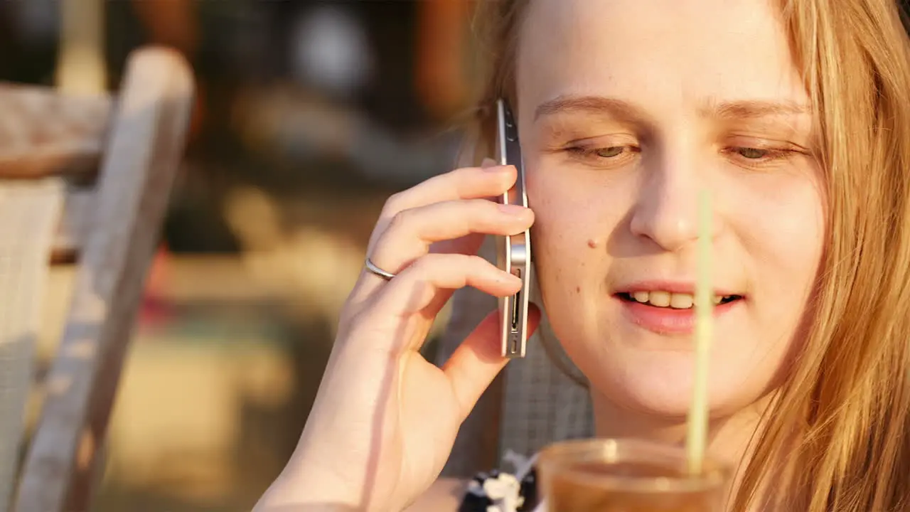 Young woman talking on mobile and drinking coffee cocktail