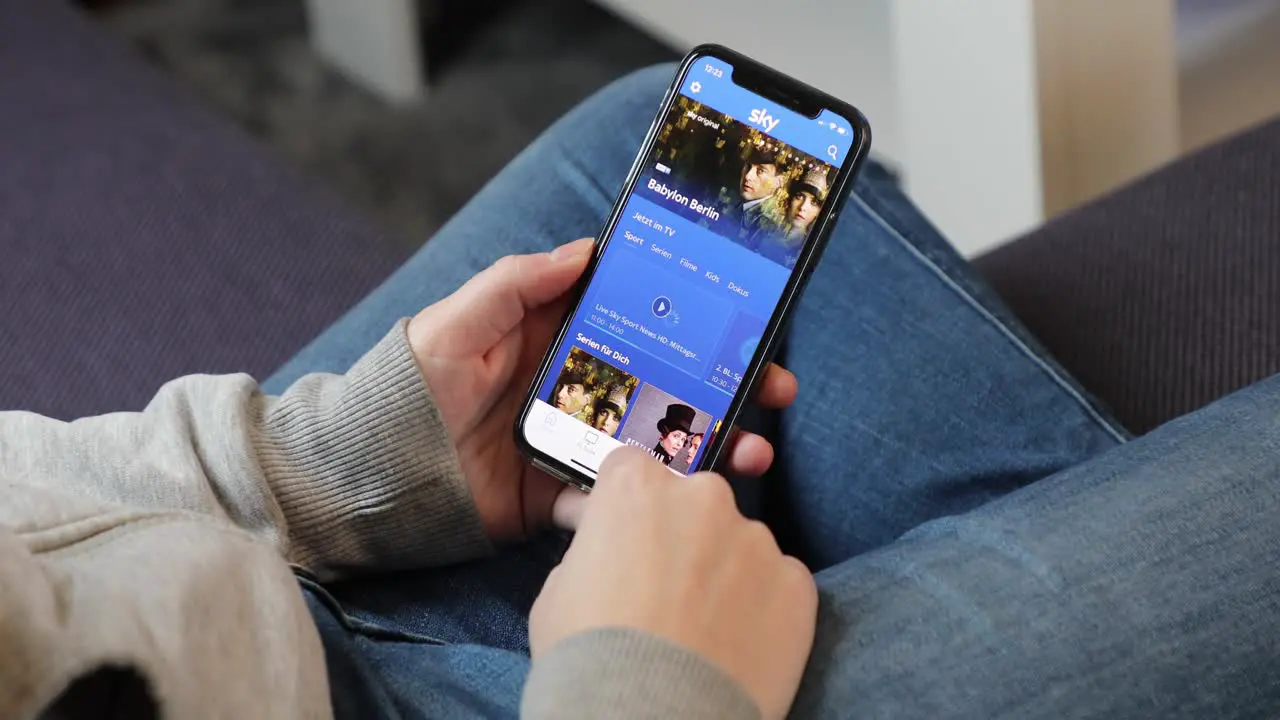 Young woman using Sky Go app on an iPhone in casual home environment