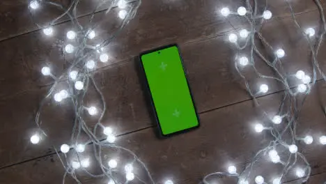 Overhead Shot Of Revolving Green Screen Mobile Phone With Christmas Decorations And Lights 2