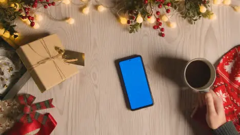 Overhead Shot Of Person With Blue Screen Mobile Phone With Christmas Decorations And Wrapping