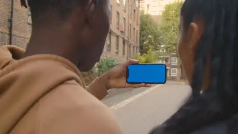 Close Up Of Young Couple Watching Sport On Blue Screen Mobile Phone In Urban City Area 