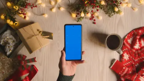 Overhead Shot Of Person Holding Blue Screen Mobile Phone With Christmas Decorations And Wrapping 2